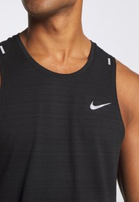 Camiseta deportiva negra sin mangas con un escote redondo, tela texturizada y un pequeño logo blanco de Nike en el lado izquierdo del pecho.
