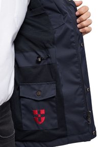 Ciemnoniebieska kurtka z siateczkową podszewką, posiadająca przednią kieszeń z zapięciem na guzik oraz czerwony haftowany logo z boku.