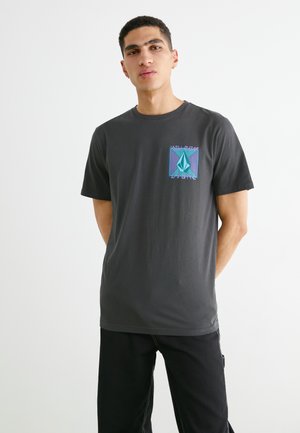 Camisa de algodón gris con cuello redondo, mangas cortas y un logo geométrico colorido en el lado izquierdo del pecho. Ajuste simple y relajado.