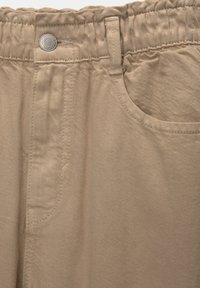 Pantalon en coton beige avec une ceinture élastique, tissu légèrement texturé, fermeture à bouton métallique et poche frontale.