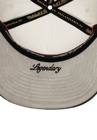 Parte inferior de una gorra gris con la palabra "Legendario" bordada en cursiva, costuras de acento rojas y una textura de tela suave. Hardware circular visible.