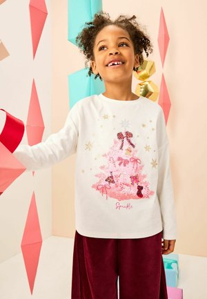 Weißes Langarmhemd mit einem rosa Pailletten-Weihnachtsbaumdesign, verziert mit Bändern und Ornamenten, kombiniert mit bordeauxroten Nadelcordhosen.