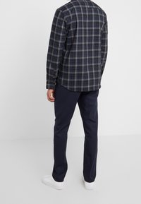 Rutig skjorta i mörkblått, svart och ljusblått, med långa ärmar och knäppningar vid ärmsluten, parat med marinblå byxor och vita sneakers.