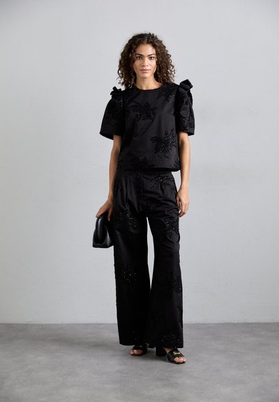 Top nero ricamato con maniche a sbuffo e pantaloni abbinati, caratterizzati da motivi floreali in perline. Tessuto liscio, vestibilità rilassata e gambe larghe.