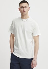 Kortermet hvit bomulls T-skjorte med avslappet passform, rund hals og raglanermer, kombinert med mørkeblå cargo-shorts.