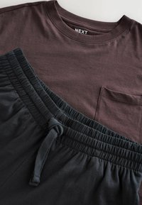 Burgunderfarvet bomulds T-shirt med brystlomme, sammen med sorte shorts med elastisk talje og snoretræk. Flad liggende arrangement.