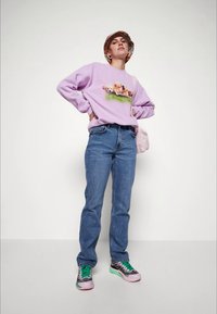 Asmuo, vilkintis alyvinės spalvos džemperį su šuniukais, mėlynus džinsus, žalius ir rožinius sportbačius, margą kibirėlį ir šviesiai rožinę petinę rankinę.