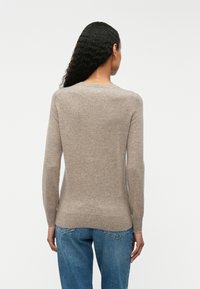 Pull en maille marron clair à manches longues, col rond, texture douce, cintré à la taille, associé à un jean bleu ; design minimal.