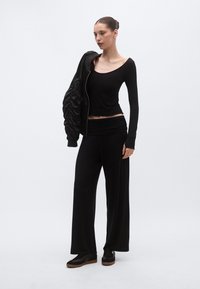 Μαύρο πουκάμισο με μακριά μανίκια και παντελόνι με φαρδιά μπατζάκια από μαλακό ύφασμα, στιλισμένο με μαύρο φουσκωτό μπουφάν με ραφές. Μαύρα παπούτσια με καστανές σόλες.