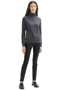 Grauer Rollkragenpullover aus weichem Stoff mit langen Ärmeln, kombiniert mit schwarzen Skinny-Hosen und schwarzen Schnürschuhen.