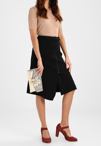 Mustat A-linjaiset hameet, joissa on edessä vetoketju, yhdistetty ribattuun beigeen toppiin. Asusteena metallinen laukku ja punaiset korot nilkkaremmillä.