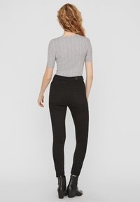 Šedý žebrovaný top s krátkým rukávem doplněný vysokými černými skinny džíny a kotníkovými botami, který předvádí přiléhavou siluetu a hladkou texturu.
