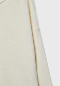 Cremfarbener Strickpullover mit lockerer Passform, der einen strukturierten Stoff, überschnittene Schultern und ein schlichtes Design bietet.