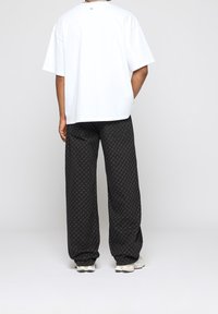 T-shirt blanc à manches courtes et pantalon noir à motifs avec un design répétitif subtil ; coupe décontractée avec taille élastique ; chaussures de sport.