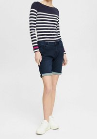 Top de rayas azul marino y blanco de manga larga, combinado con shorts de mezclilla oscuros y remangados. Zapatillas blancas. Conjunto casual con texturas mixtas.