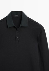 Schwarzes Poloshirt mit einfarbigem, geripptem Design, drei Knöpfen und einem kontrastierenden Kragen in einem dunkleren Farbton.