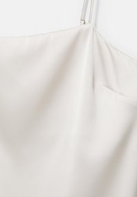 Caraco en satin blanc avec fines bretelles ajustables et une petite poche visible sur le côté droit.
