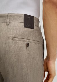 Lichtbruine linnenmixbroek met een achterzak, knoopsluiting en een donkere leren merklabel met de opdruk "JOOP!" op de tailleband.