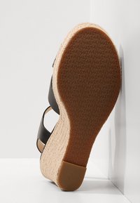 Sandale compensée avec des lanières en cuir noir, une plateforme en jute tissé et une semelle en caoutchouc marron avec un motif texturé pour une meilleure adhérence.