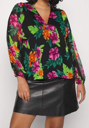 Kvinde iført en sort bluse med farverige pink, orange og grønne blomsterprint og en sort lædermininederdel.