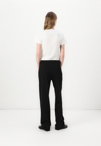 T-shirt bianca e pantaloni neri indossati da una persona, che mostrano un design semplice con un colore uniforme, vestibilità dritta e dettagli minimi.