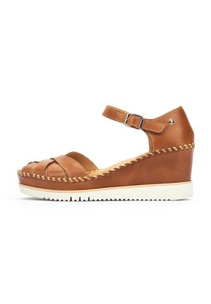 Sandalias de cuña de cuero marrón con parte superior trenzada, correa ajustable en el tobillo y suela de goma blanca. Presenta un acabado texturizado y detalles de costura.