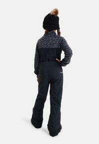 Niebiesko-szary polarowy sweter z wzorzystą górną częścią, w połączeniu z czarnymi spodniami narciarskimi. Dziana czarna czapka z akcentującym pomponem z futra.