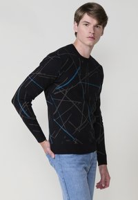 Suéter negro con un patrón geométrico en líneas grises y azules. Confeccionado en un material suave, presenta un cuello redondo y puños acanalados.