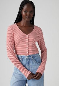 Röd och vit randig långärmad topp med v-ringning och knappstängning, kombinerad med högmidjade blå denimjeans.