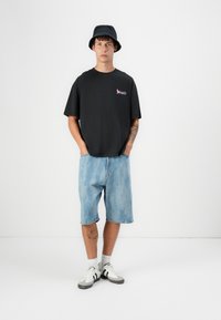 Svart T-skjorte med korte ermer og liten rosa grafikk, kombinert med lyseblå denimshorts, bøttehatt og joggesko. Lekkert hverdagsantrekk.