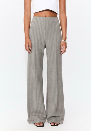 Pantalons larges gris avec une texture en côtes verticales, taille haute et une coupe fluide. Associés à un haut court blanc et des sandales noires.