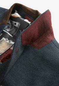 Mørk denimjakke med en bordeauxfarvet krave, struktureret stof og et mønstret indre med vintage fotografiudskrifter.