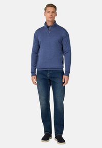 Pull en tissu doux, bleu marine, à zip quart, associé à un jean bleu classique et des chaussures décontractées sombres, porté par un modèle masculin debout.