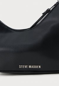 Geantă sintetică neagră cu o textură netedă, formă curbată și logo-ul argintiu "Steve Madden". Prezintă un design simplu și curea ajustabilă.