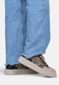 Sneakers w leopardzim wzorem i czarnymi oraz różowymi akcentami, wykonane z teksturowanej zamszowej i kanwasowej tkaniny, w zestawieniu ze postrzępionymi niebieskimi dżinsami.