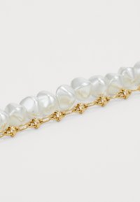 Pearl bracelet with irregular-shaped white pearls strung on a gold-tone chain, featuring small knot-like accents between the pearls.