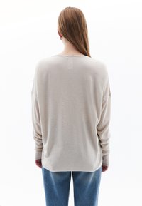 Camiseta de manga larga color beige claro con un corte relajado, escote redondo y puños acanalados, combinada con pantalones de denim holgados. Textura suave.