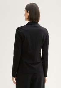 Black tailored blazer with long sleeves, smooth texture, notched collar, and structured shoulders. Features minimal stitching detail.