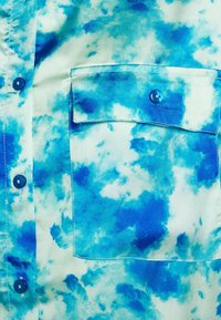 Camicia a maniche corte realizzata in tessuto leggero, caratterizzata da un motivo tie-dye blu e acquamarina, chiusura con bottoni e taschino sul petto.