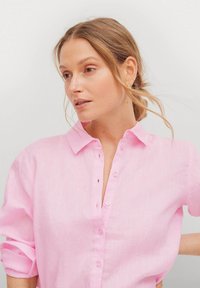 Camicia di lino rosa chiaro con chiusura a bottoni, colletto e maniche arrotolate, caratterizzata da una leggera trama e una vestibilità rilassata.