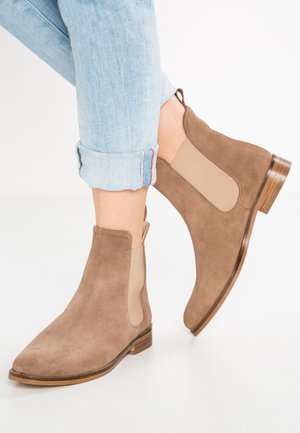 Jean bleu clair roulé porté avec des bottines Chelsea en daim beige, dotées de panneaux élastiques latéraux et de petits talons en bois.