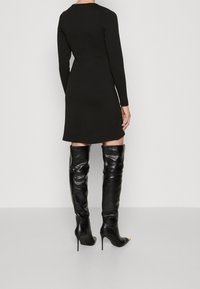 Svart långärmad klänning med en figurnära silhuett och mid-thigh längd, parat med höga svarta läderstövlar som går upp till låren. Slät textur.