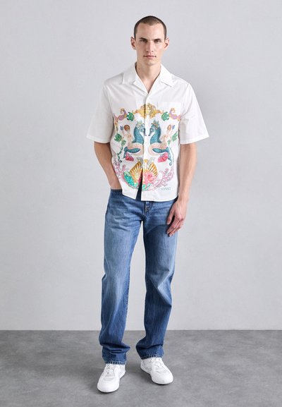 Short-sleeve white shirt with colorful aquatic-themed pattern; worn with light blue jeans and white sneakers.
