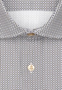 Camicia da uomo con colletto su sfondo bianco, caratterizzata da un piccolo motivo circolare in blu navy e beige, chiusura anteriore con bottoni e texture liscia.