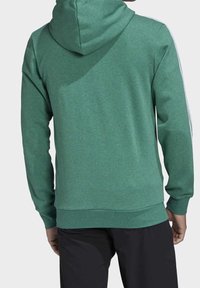 Sudadera con capucha verde de tejido texturizado, con mangas largas y cintura acanalada. Incluye rayas blancas a lo largo de los hombros.