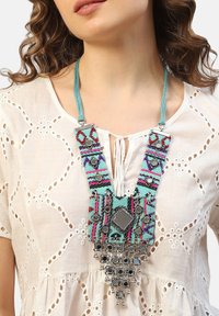 Vícecenný textilní náhrdelník s geometrickým vzorem, se tyrkysovými, růžovými a stříbrnými akcenty. Stříbrně tónované komponenty na základně.