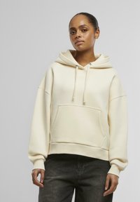 Kremfarget hettegenser i myk stoff med frontlomme, snøring i hetten og ribbede mansjetter. Oversized design med avslappet passform.