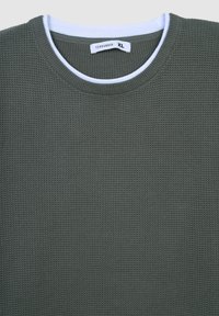 Oliwkowy sweter o fakturze z okrągłym dekoltem i białym wewnętrznym kołnierzykiem. Metka mówi "Terranova", rozmiar XL. Szczegółowy wzór w wafelkowym splocie.