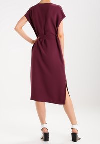 Bordeaux Midi-Kleid mit lockerer Passform, kurzen Ärmeln und gebundenem Taillenband. Verfügt über einen seitlichen Schlitz und glattes Material. Kombiniert mit Sandalen mit dicken Absätzen.
