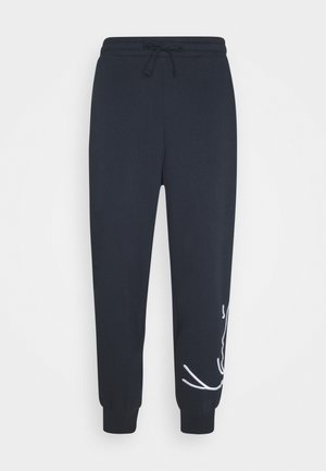 Pantaloni de trening bleu marin, confecționați dintr-un material moale, având un talie elastică cu șnur și un design grafic alb pe piciorul stâng.